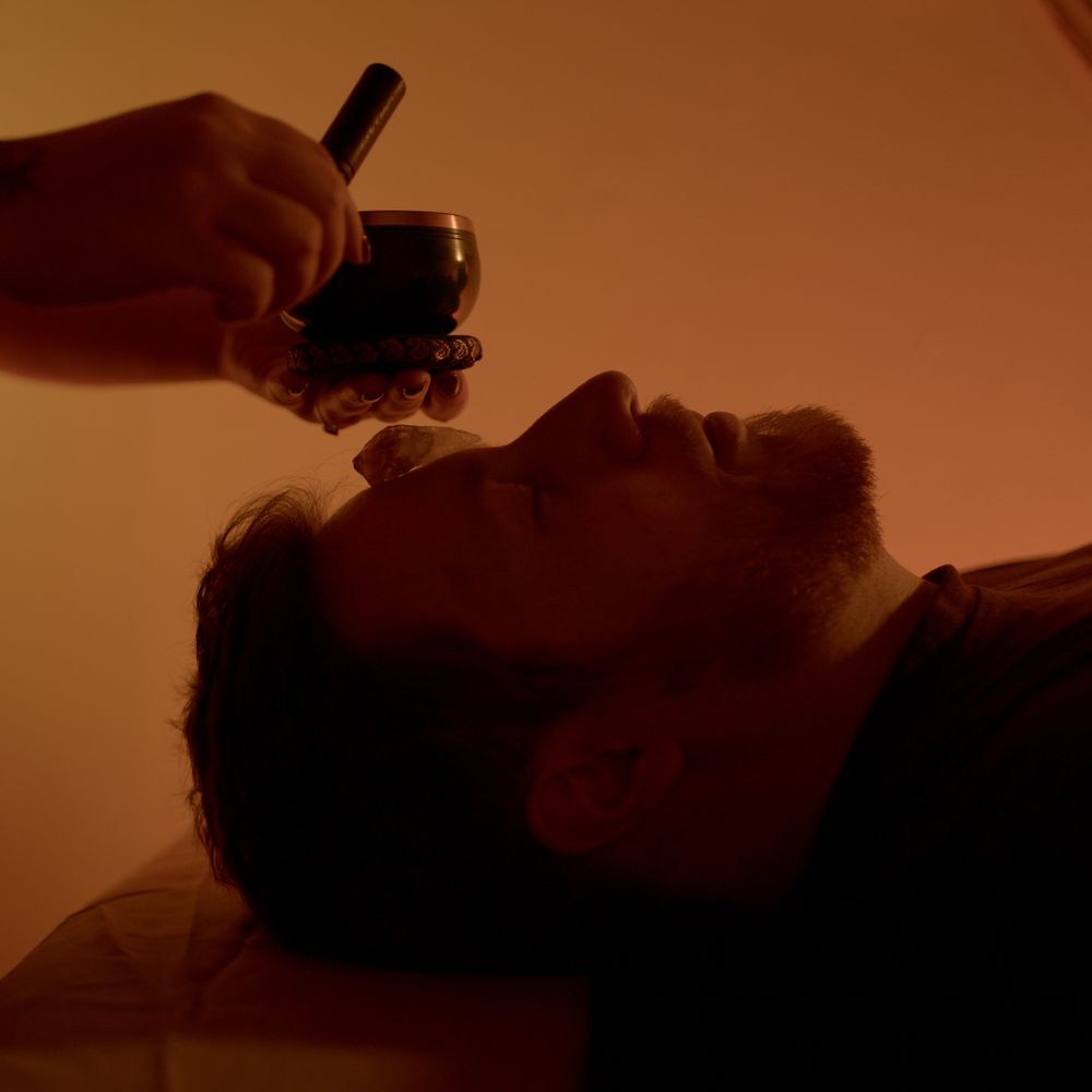 A singing bowl held over a client resting with their eyes closed