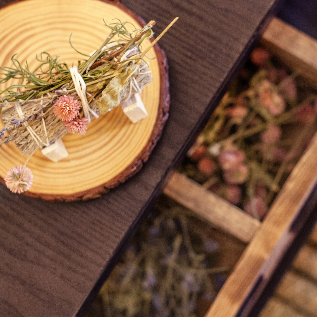 A handmade sage bundle with dried flowers on a wood slice